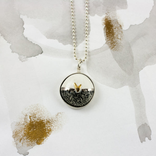 White oval shaped silver pendant with a golden heart