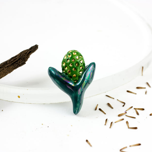 Tamsiai žalios spalvos sagė su perlų blizgesiu ir aukso liustro dėmelėmis